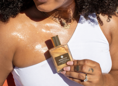 Woman holding NeoraGlow Illuminating Body Oil in front of her chest with the body oil smeared across her décolletage